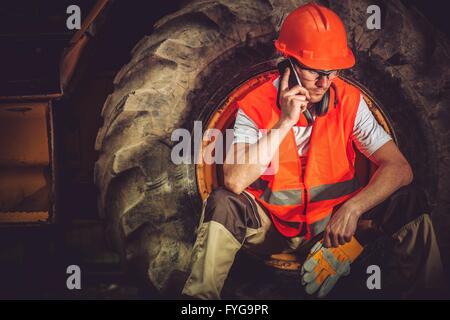 Hard Construction Business Concept with Caucasian Businessman Making Business Call While Seating Inside Heavy Duty Bulldozer Tir Stock Photo