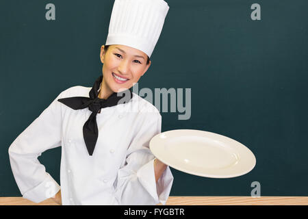 Composite image of smiling female cook holding empty plate in kitchen Stock Photo