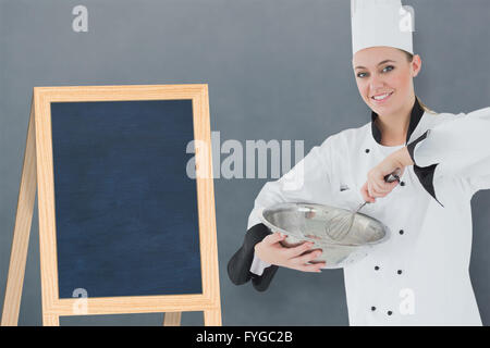 Composite image of happy female chef holding wire whisk and mixing bowl Stock Photo