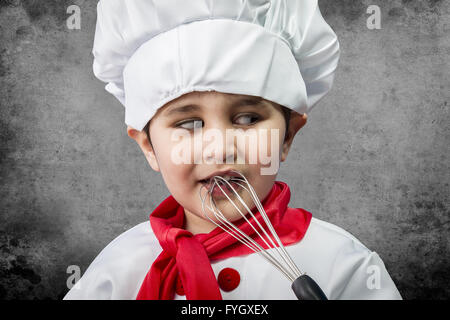 Little boy cook in uniform over vintage  background playing with cookware Stock Photo