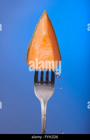 Melon fruit piece on fork with water drops and empty blue background concept photo. Ideal for healthy eating campaign. Stock Photo