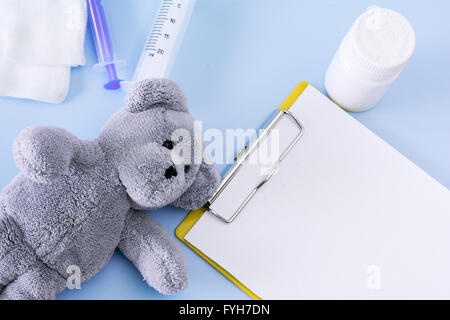 Medical conceptual picture with pills, teddy bear, injection, gauze, bottle, empty clipboard sheet. Stock Photo