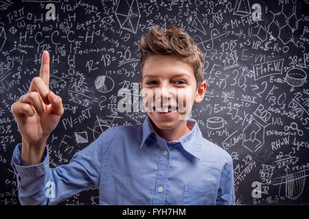 Boy with raised finger against big blackboard with formulas Stock Photo