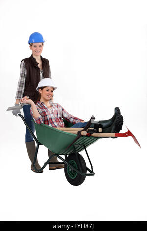 Female builder pushing colleague in wheelbarrow Stock Photo