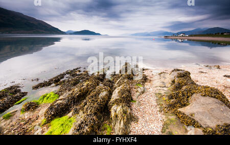 A Rocky shore and pebble beach reaches into Loch Linnhe sea loch at Onich near Glencoe in the Highlands of Scotland, with mounta Stock Photo