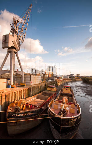 London, England - April 11, 2010: Two barges docked at a wharf on a small river. A crane and cargo occupy the wharf. Stock Photo