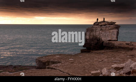 A pair of climbers silhouetted against the sunset stand on Pulpit Rock at Portland Bill in Dorset, England. Stock Photo