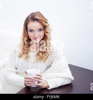Young woman at home drinking hot coffee, wrapped in a scarf,  white background, place for your text Stock Photo