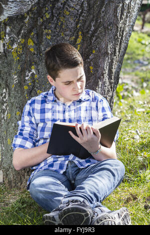 Young boy reading a book in the woods with shallow depth of field and copy space Stock Photo