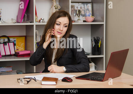 Business woman in office talking on phone looking at monitor Stock Photo