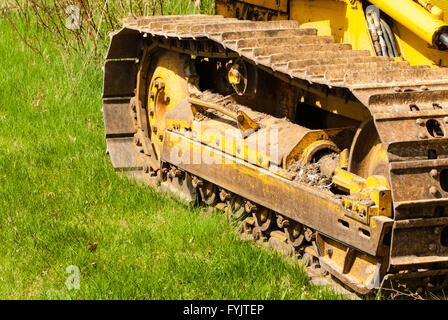 Muddy caterpillar tracks and treads on bulldozer parked on green grass.