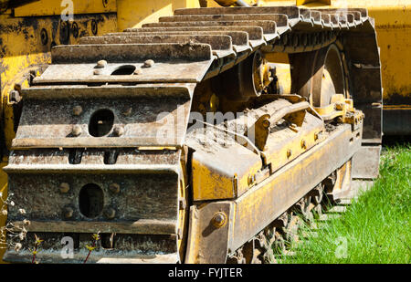 Detail of muddy caterpillar tracks and treads on bulldozer parked on green grass.