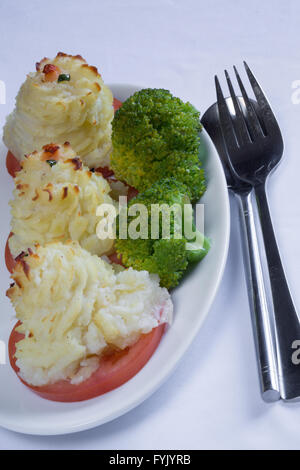 A serving of homemade Duchess Potatoes on griddled Tomato with a side of steamed Broccoli. Stock Photo