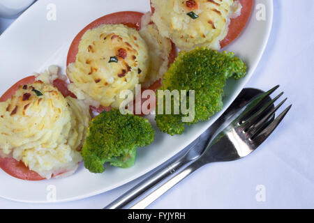 A serving of homemade Duchess Potatoes on griddled Tomato with a side of steamed Broccoli. Stock Photo
