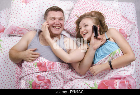 Young couple talking on the phone lying in bed Stock Photo