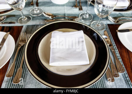 First person perspective view on neatly arranged dining table setting with folded napkin in middle of plate with utensils on sid Stock Photo