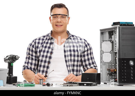 Cheerful PC technician sitting at a table and repairing a computer isolated on white background Stock Photo
