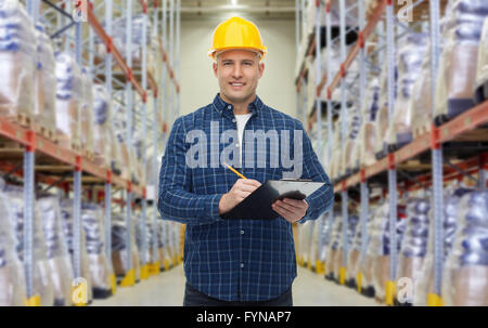 happy man in helmet with clipboard at warehouse Stock Photo