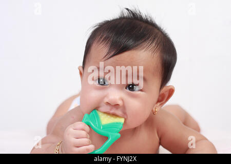 Portrait of cute little Asian baby girl lying down on bed and biting rubber toy Stock Photo