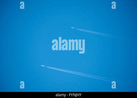Planes Contrails Blue Sky | WASHINGTON D.C., United States — Two jet aircraft cross a clear blue sky in parallel, each trailing a sharp white contrail. Contrails form when hot, humid engine exhaust condenses and freezes in the cold, low-pressure air at cruising altitudes above roughly 26,000 feet (8,000 m). The paired, near-identical trails suggest similar flight paths and altitudes, a common sight over air corridors near a major metropolitan region. Stock Photo