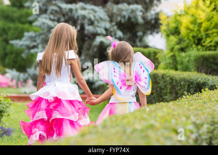 Two little girls, princess and fairy, walk hands in the garden Stock Photo