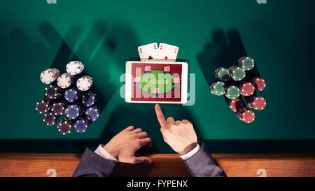 Poker player's hands with digital tablet, stacks of chips and cards on green table, top view Stock Photo