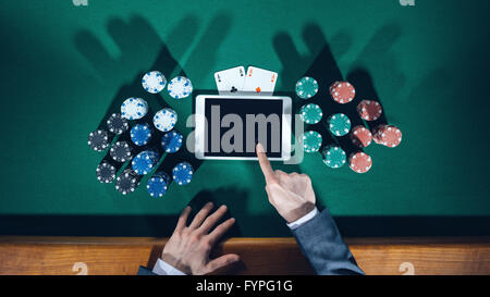 Poker player's hands with digital tablet, stacks of chips and cards on green table, top view Stock Photo