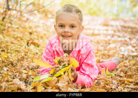 Six year old girl lying on the yellow fallen leaves Stock Photo
