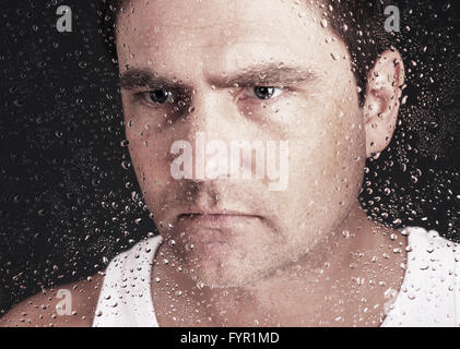 Closeup of pensive man looking through window covered with raindrops Stock Photo