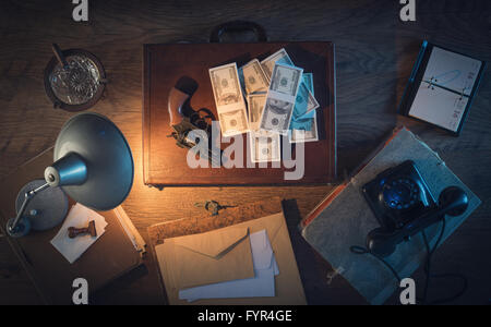 Vintage desktop in the dark with a gun, a briefcase and a lot of dollar packs, top view Stock Photo