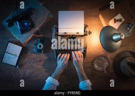 Vintage journalist's desk 1950s style, he is working and typing on his typewriter late at night, top view Stock Photo