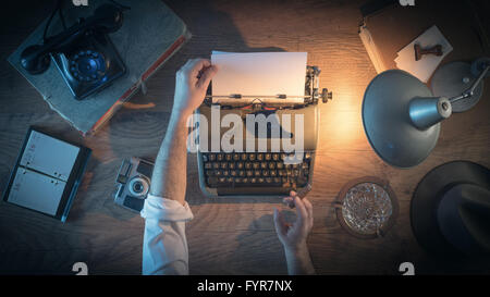 Vintage journalist's desk 1950s style, he is working and typing on his typewriter late at night, top view Stock Photo