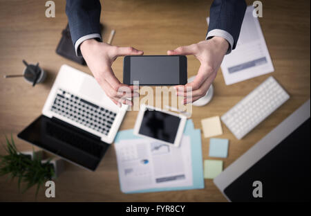 Businessman working at office desk hands top view with laptop and financial reports: he is using a mobile touch screen smart pho Stock Photo