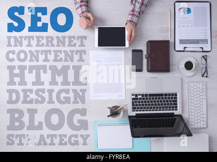 Businessman working at office desk and using a digital touch screen tablet, seo and web text concepts on left side, top view Stock Photo