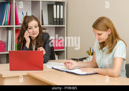 Manager shocked looking at laptop and talking on a cell phone, an employee of the office wrote in a document Stock Photo