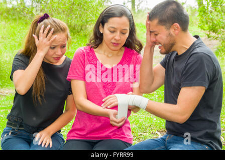 Young man with injured wrist sitting and getting bandage compression wrap from female, outdoors environment Stock Photo