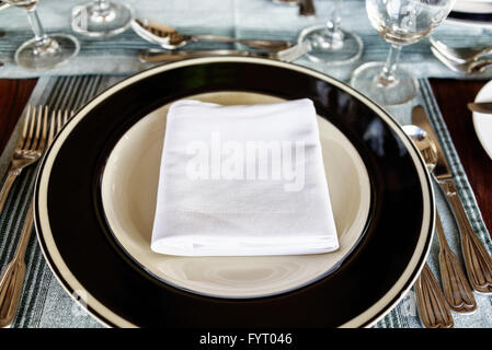 First person perspective view on neatly arranged dining table setting with folded napkin in middle of plate with utensils Stock Photo