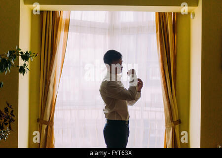 Elegant young fashion man in white shirt looking at his cufflinks while fixing them Stock Photo
