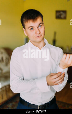 Elegant young fashion man in white shirt posig front of the camera while fixing cufflinks Stock Photo