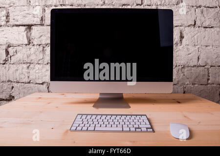 Wooden desk with computer, keyboard and mouse. Brick wall. Stock Photo