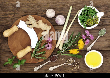Herb and spice selection with chopper and board, mortar with pestle and olive oil on old oak background. Stock Photo