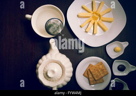 Plates of buiscuits and cheeses organized in star formation on dark wooden surface next to tea kettle, small plates with jam plus butter, shot from above angle Stock Photo