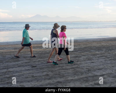 Three tourists walking on the beach early in the morning in Jimbaran Bay, Bali. Stock Photo