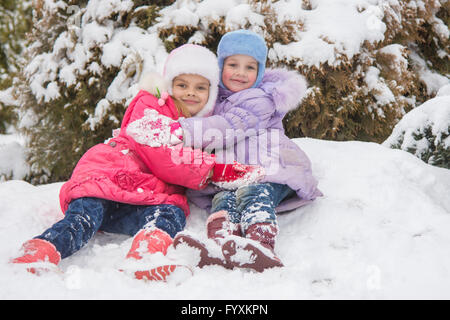 Two girls are sitting in a snowdrift snow and hugging each other Stock Photo