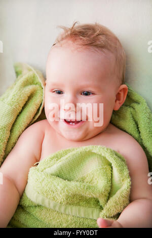 A happy baby lying on bed in green towel Stock Photo