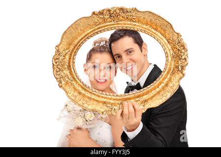 Young newlywed couple posing behind a vintage picture frame and smiling isolated on white background Stock Photo