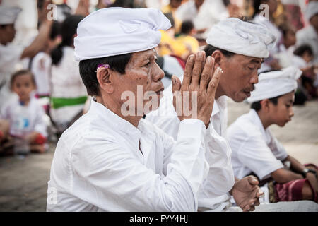 Balinese man dressed in ceremonial clothes prays with hands together at a temple on the Indonesian island of Bali at Kuningan Stock Photo