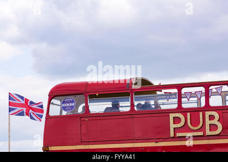 Red London Transport Pub bus Hop On Inn with Union Jack flag flying in the wind at St Georges Day Festival in Poole, Dorset, UK Stock Photo