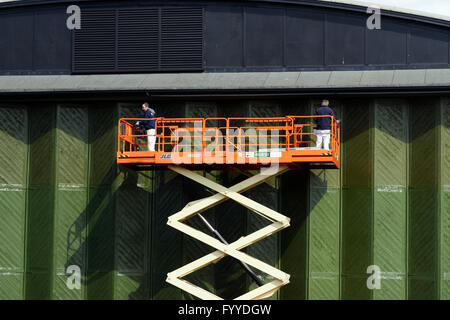 Two men on a scissor lift painting large hangar doors Stock Photo