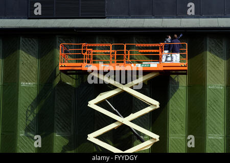 Two men on a scissor lift painting large hangar doors Stock Photo